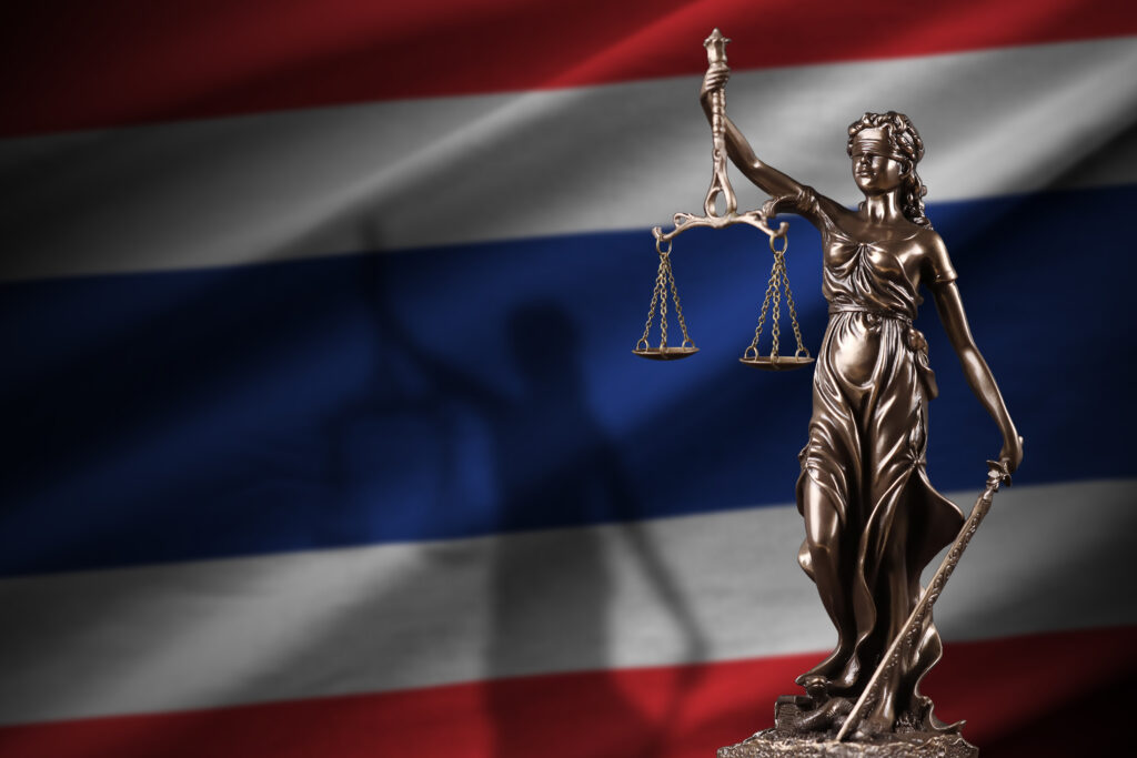 Thailand flag with statue of lady justice and judicial scales in dark room. Concept of judgement and punishment